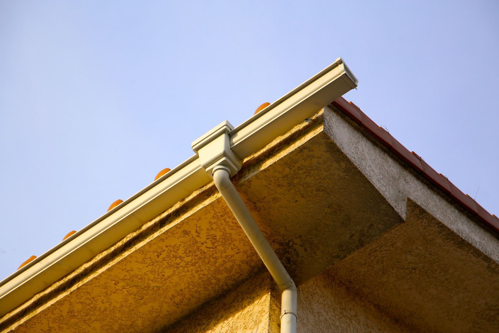 Close-up of a house roof eave with gutter against a clear blue sky