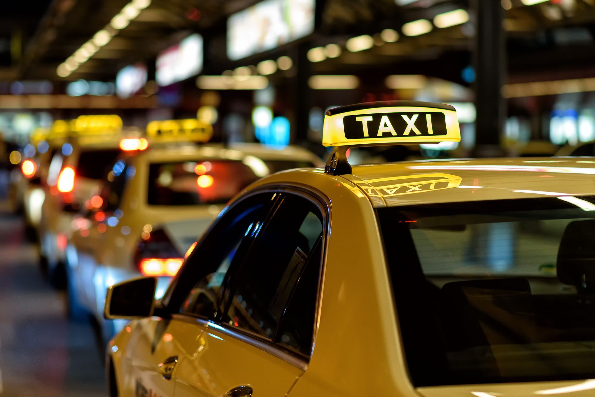 Des taxis jaunes alignés, panneaux lumineux indiquant TAXI, stationnés la nuit.
