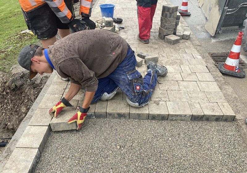 ein Mann kniet auf dem Boden und legt Steine auf einen Bürgersteig