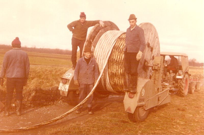 eine Gruppe von Männern steht neben einem großen Schlauch und einem Traktor