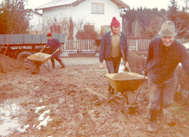 drei Männer schieben schubkarren im Schlamm vor einem Haus