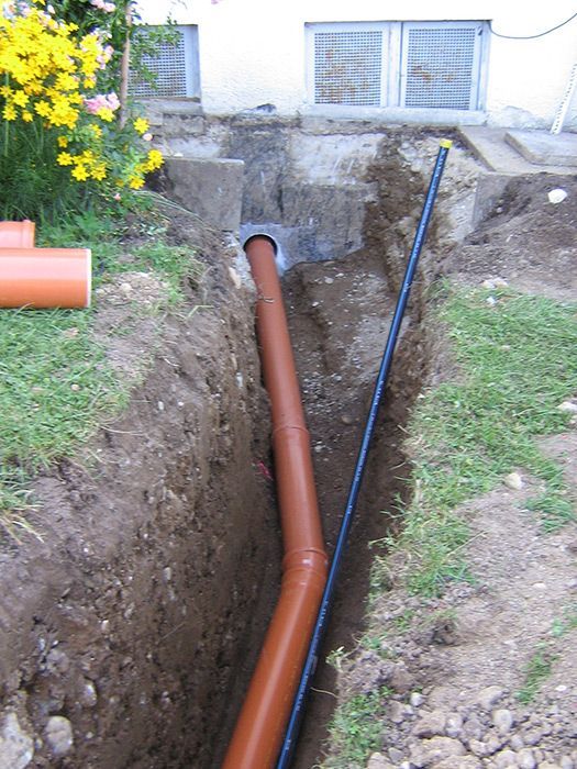 ein braunes Rohr in einem Graben mit einem schwarzen Rohr davor