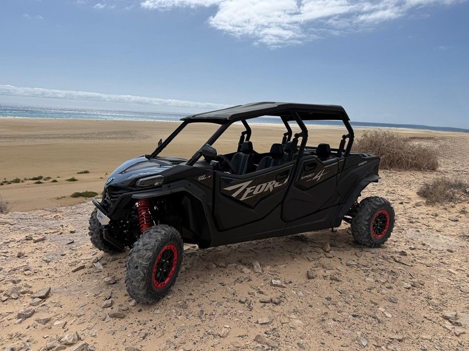 UTV todoterreno negro con ruedas rojas estacionado en una duna rocosa del desierto bajo un cielo azul.