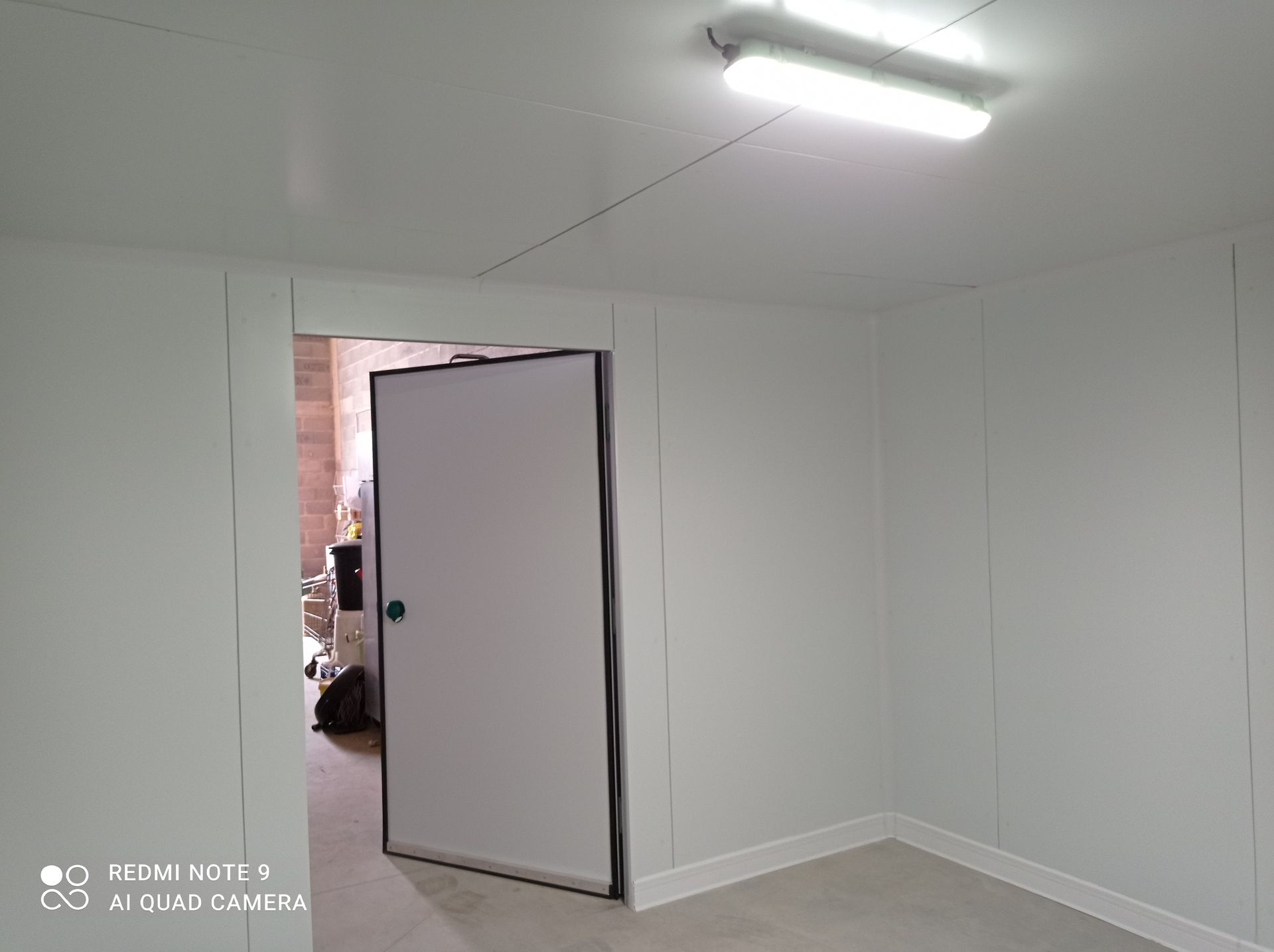 Vue intérieure d'une petite pièce blanche avec une porte entrouverte.