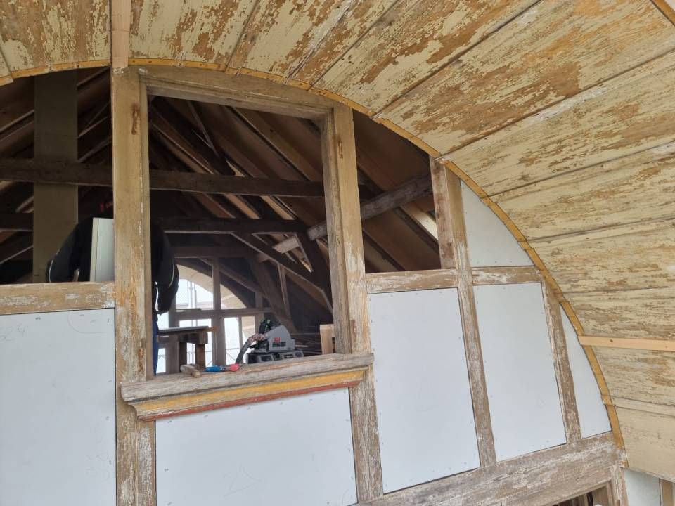 Innenwand im Bau mit freiliegendem Holzgerüst und weisser Verkleidung unter einer geschwungenen, unfertigen Decke