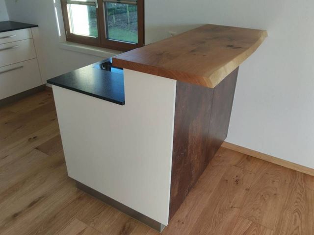 Moderne Kücheninsel mit weissem Schrank, schwarzer Arbeitsplatte und dicker Holzplatte in Metzgerblock-Optik.