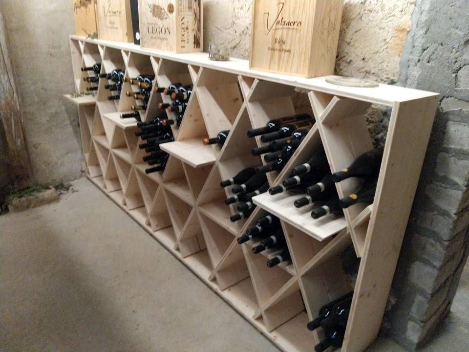 Ein hölzernes Weinregal mit in Fächern entlang einer Steinwand aufbewahrten Flaschen.