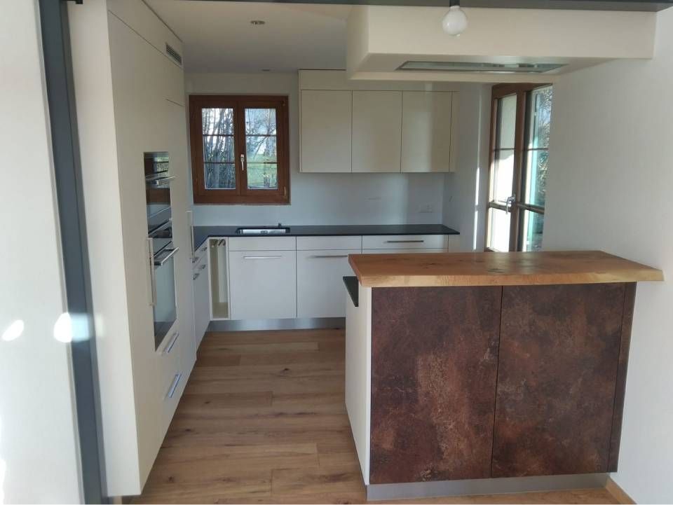 Kleine, moderne Küche mit weissen Schränken, Holzboden, Fenster und einer Kücheninsel aus Holz.