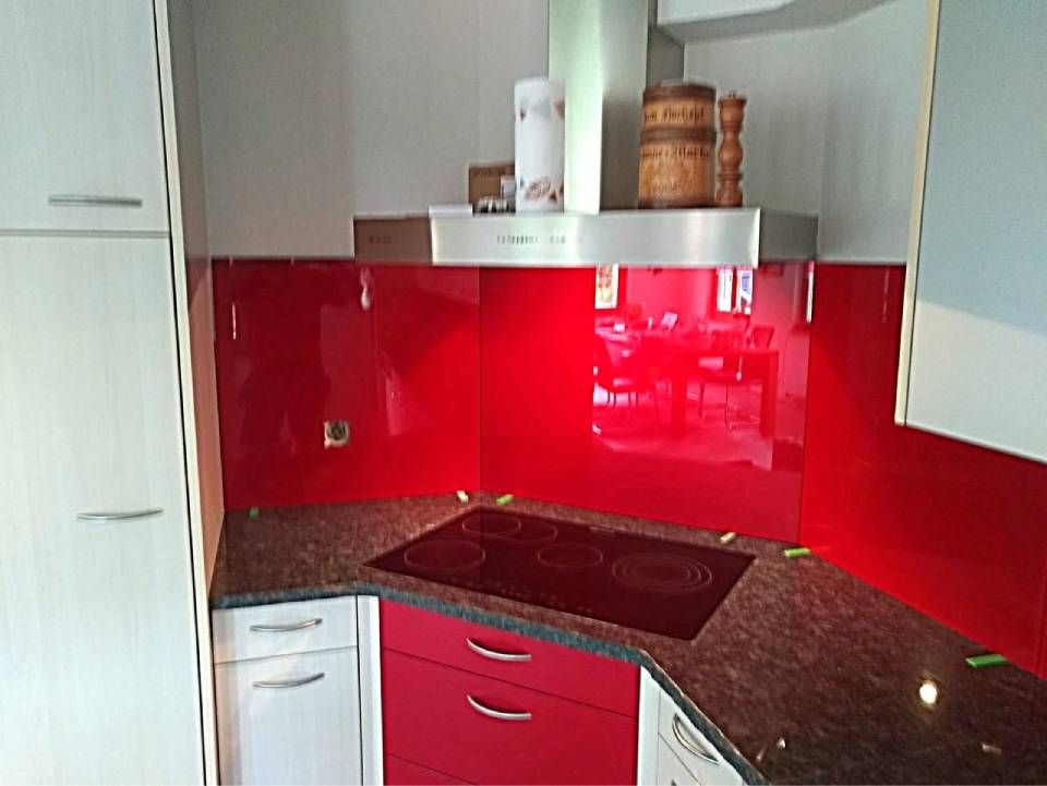 Moderne Küchenecke mit glänzend rotem Fliesenspiegel, dunkler Arbeitsplatte und weissen Schränken.