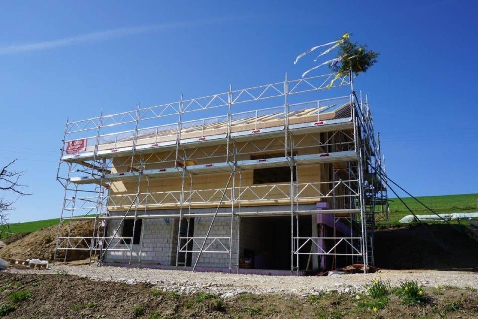 Ein im Bau befindliches Haus mit Gerüst unter blauem Himmel und vor der Kulisse eines grasbewachsenen Hügels.