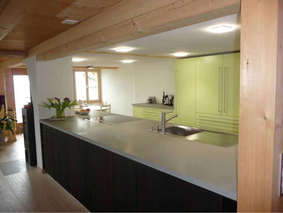 Moderne Küche mit langer Kochinsel, grünen Schränken und Holzbalken an der Decke.