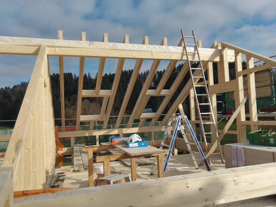 Holzrahmenhaus im Bau mit Leitern, Werkzeugen und freiliegenden Dachstühlen