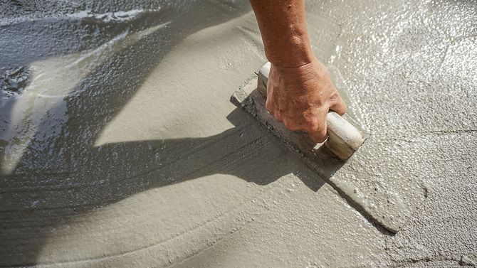 Eine Person bearbeitet einen Betonboden mit einer Kelle.