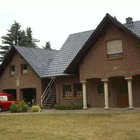 Ein roter Lieferwagen steht vor einem großen Backsteinhaus.