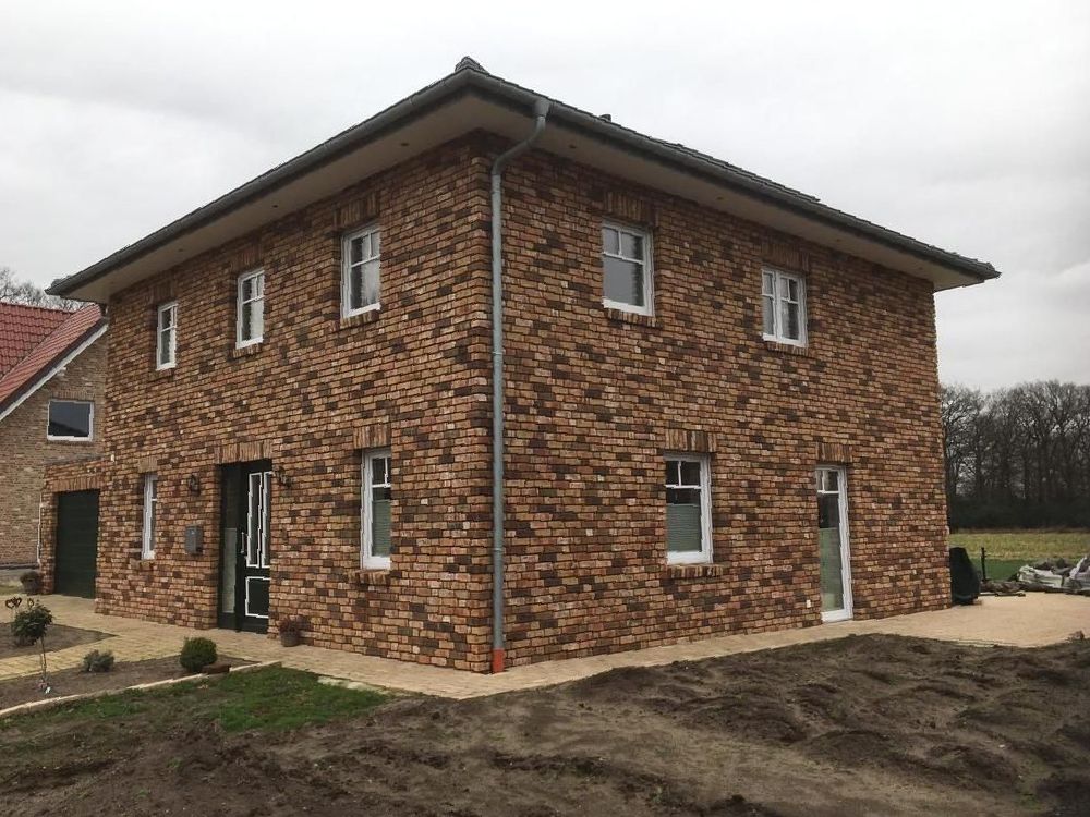Ein großes Backsteinhaus mit vielen Fenstern steht auf einem Feld.