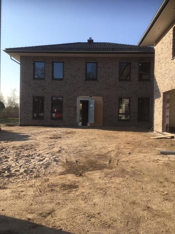 Ein großes Backsteingebäude mit vielen Fenstern und viel Erde davor.