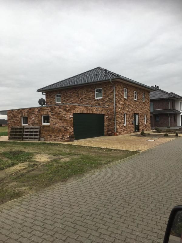 Ein Backsteinhaus mit einem grünen Garagentor und einer Satellitenschüssel auf dem Dach.