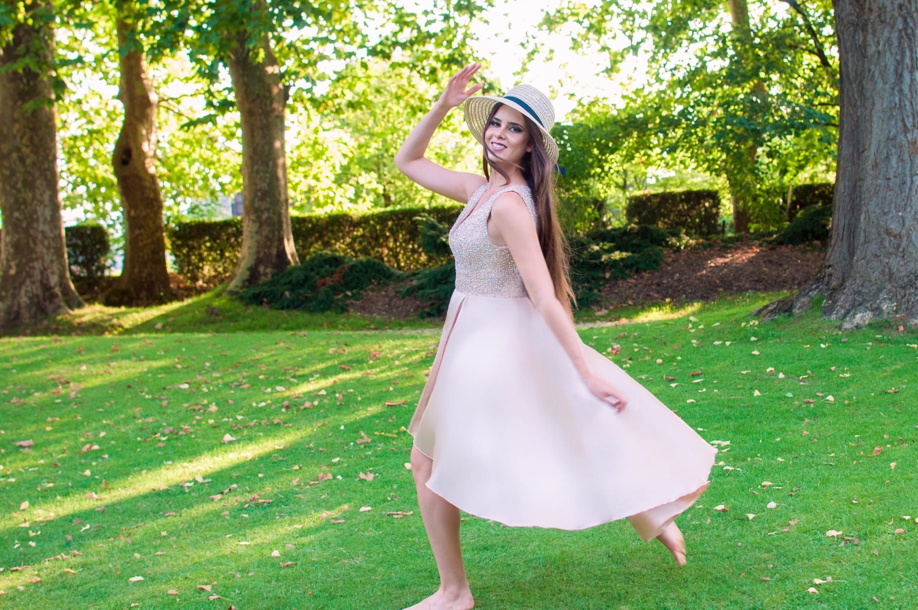 Una mujer con un vestido rosa y un sombrero está bailando en un parque.