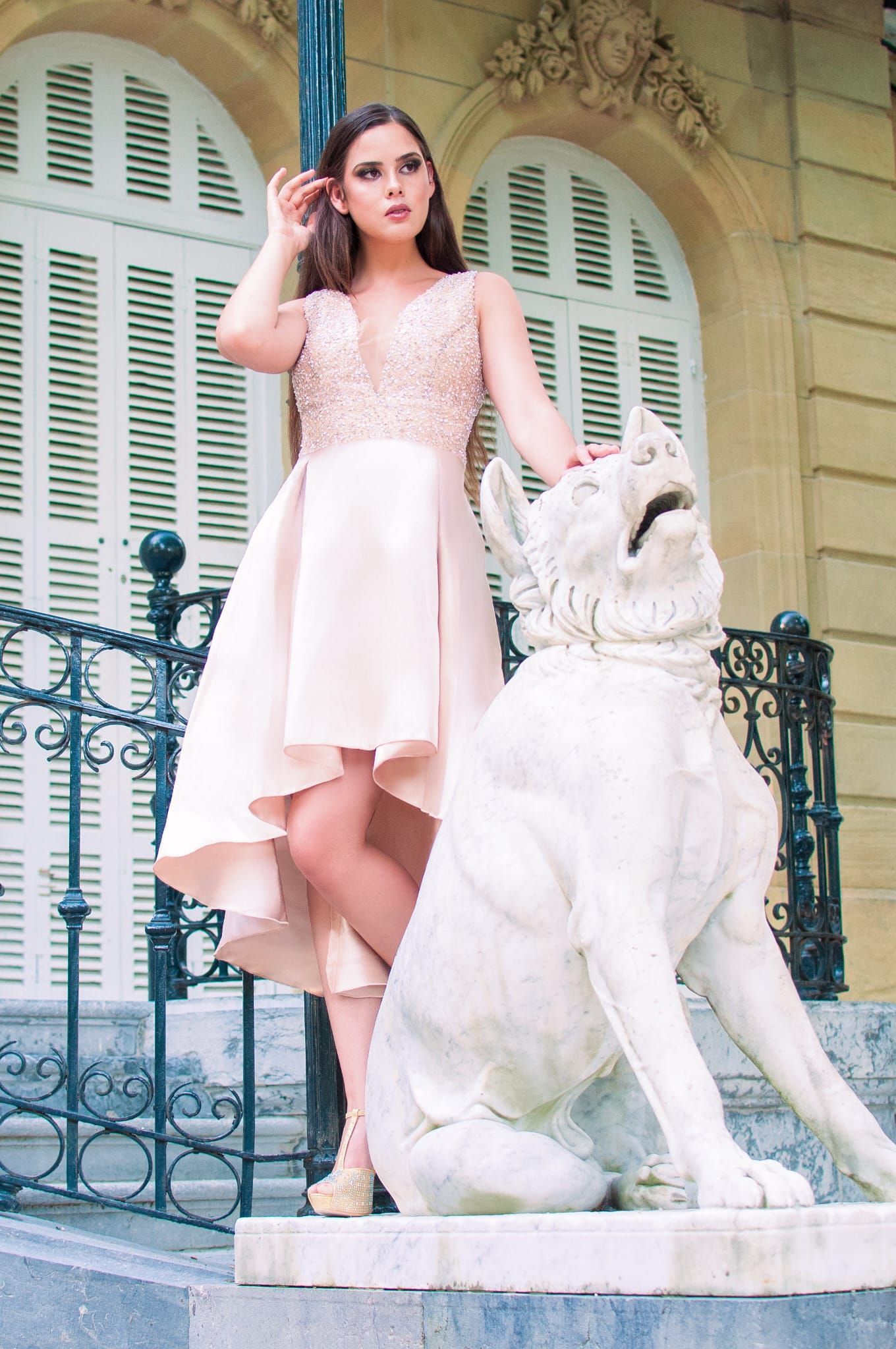 Una mujer con un vestido alto y bajo está parada junto a una estatua de un perro.