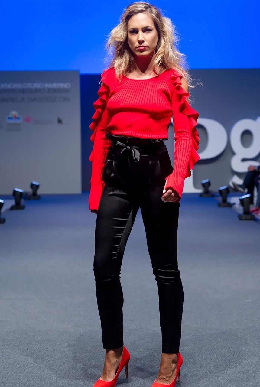 Una mujer camina por una pasarela con un suéter rojo y pantalones negros.