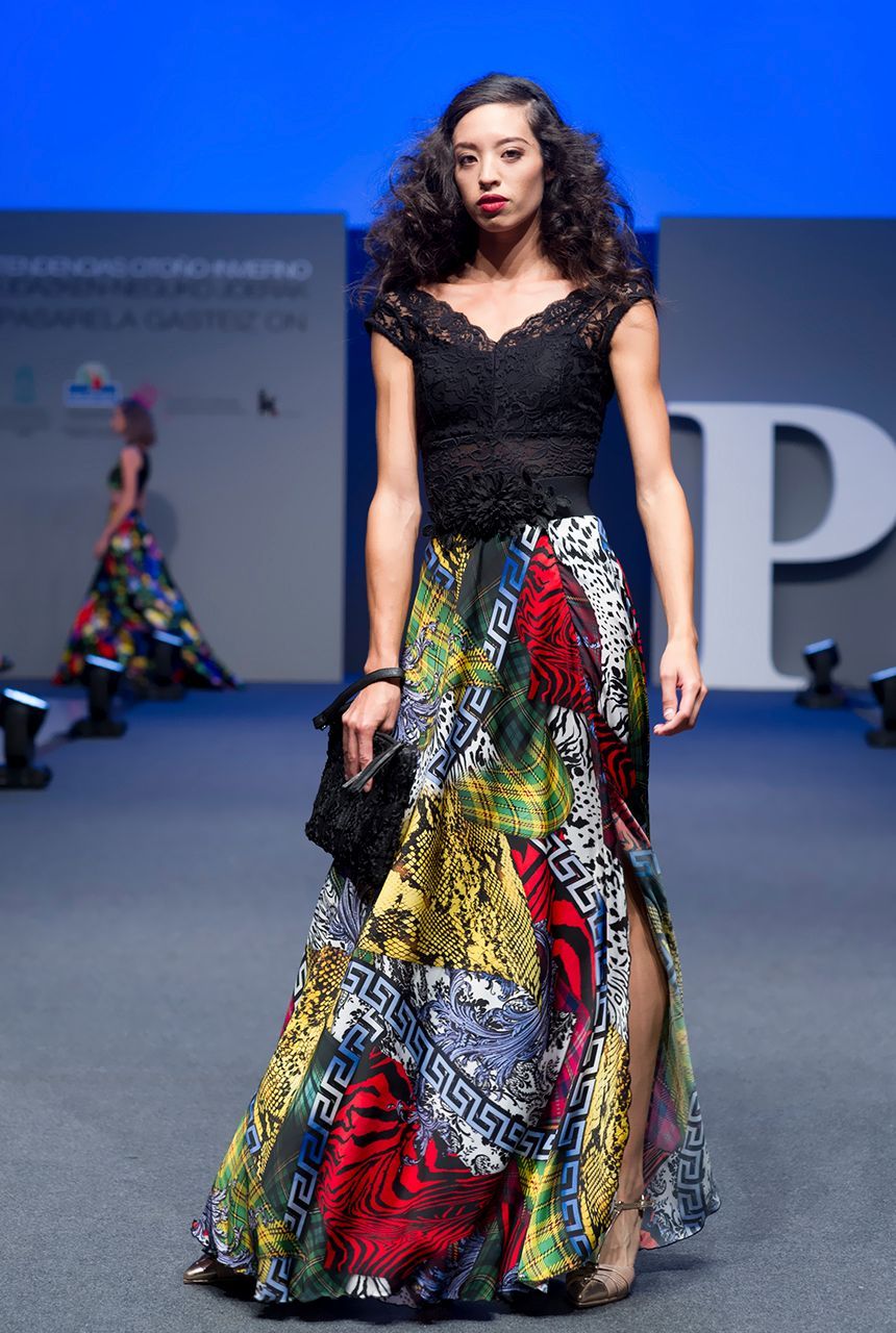 Una mujer camina por una pasarela vistiendo un top negro y una falda colorida.