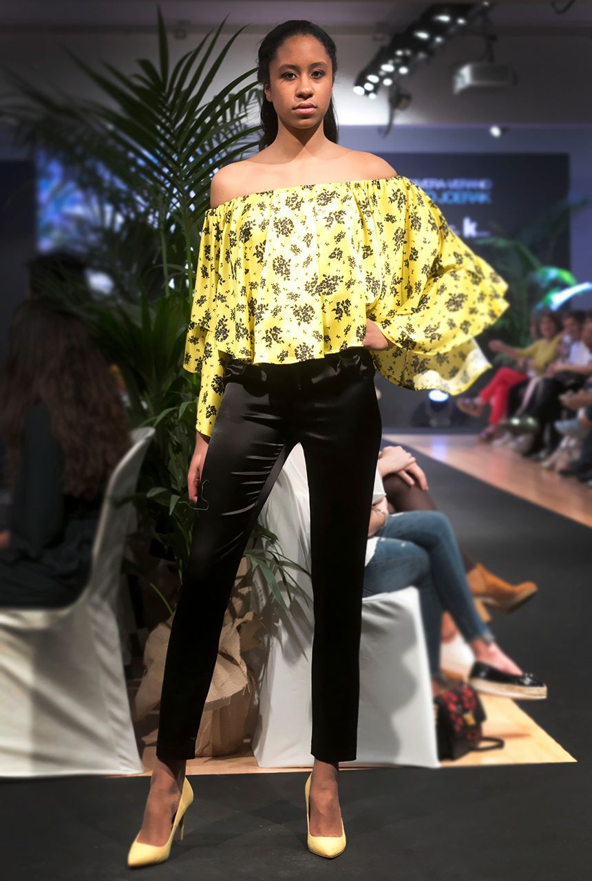 Una mujer que lleva una blusa amarilla con hombros descubiertos y pantalones negros.