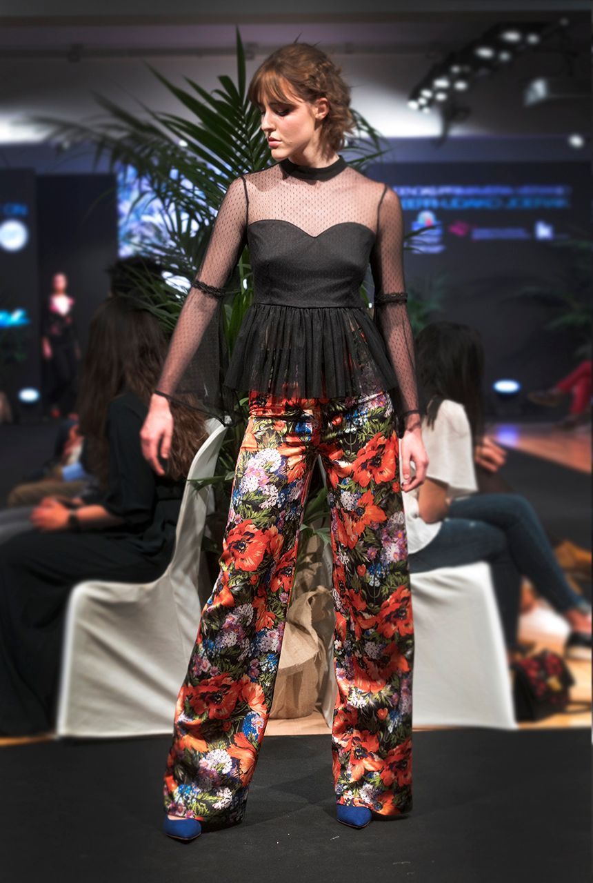 Una mujer camina por una pasarela vistiendo un top negro y pantalones floreados.