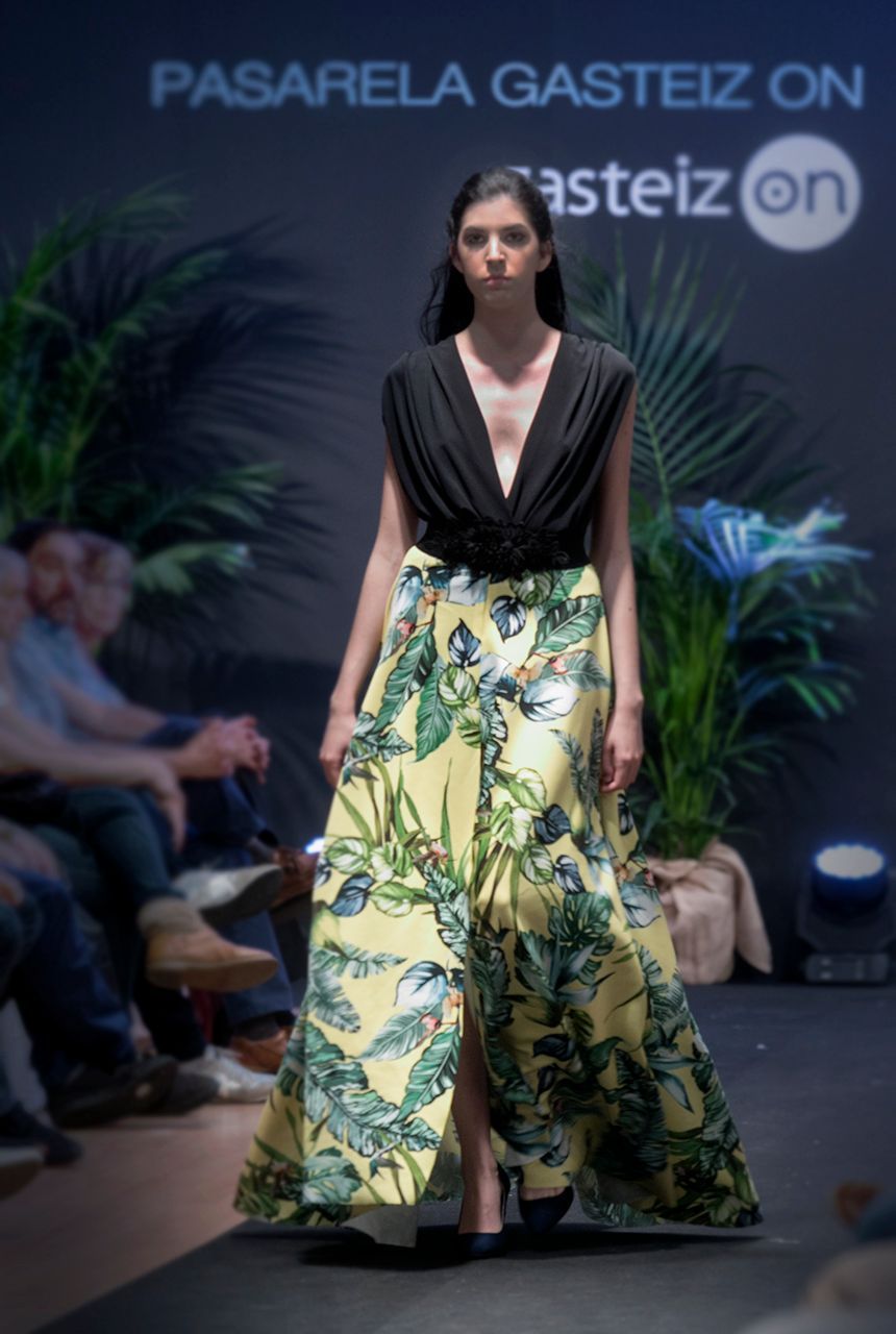 Una mujer camina por una pasarela con un top negro y una falda amarilla.