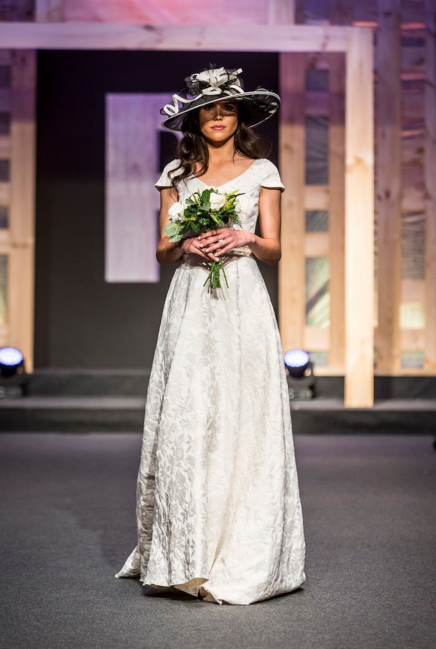 Una mujer con vestido de novia y sombrero sostiene un ramo de flores.