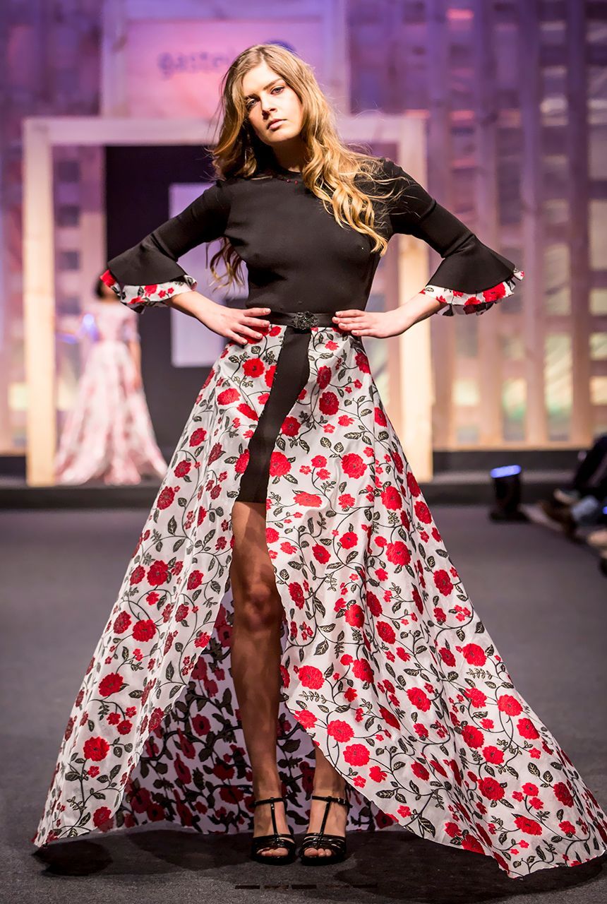 Una mujer camina por una pasarela vistiendo un top negro y una falda floral roja y blanca.