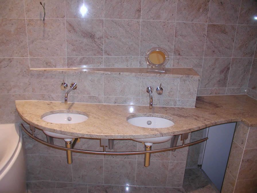 Badezimmer mit zwei Waschbecken, Granitarbeitsplatte, bronzenen Armaturen, beigen Fliesen und Spiegel.