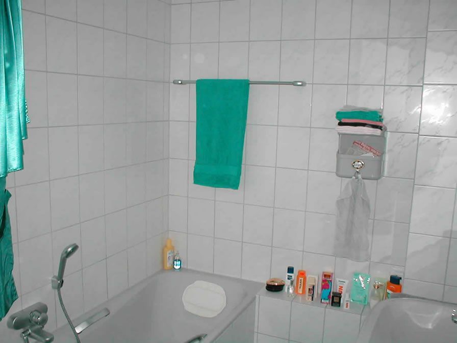 Badezimmer mit weiß gefliesten Wänden, einer Badewanne und einem hängenden blaugrünen Handtuch.