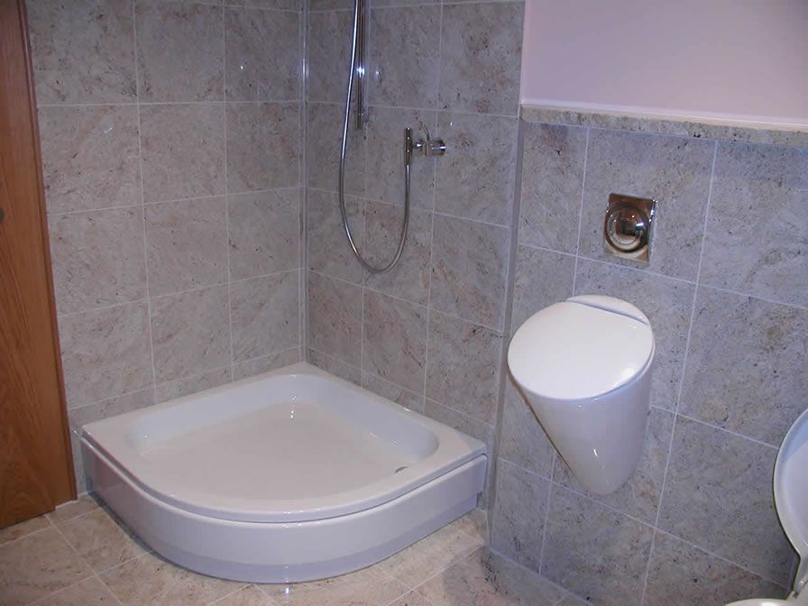 Ein kleines, gefliestes Badezimmer mit Eckdusche und Urinal.