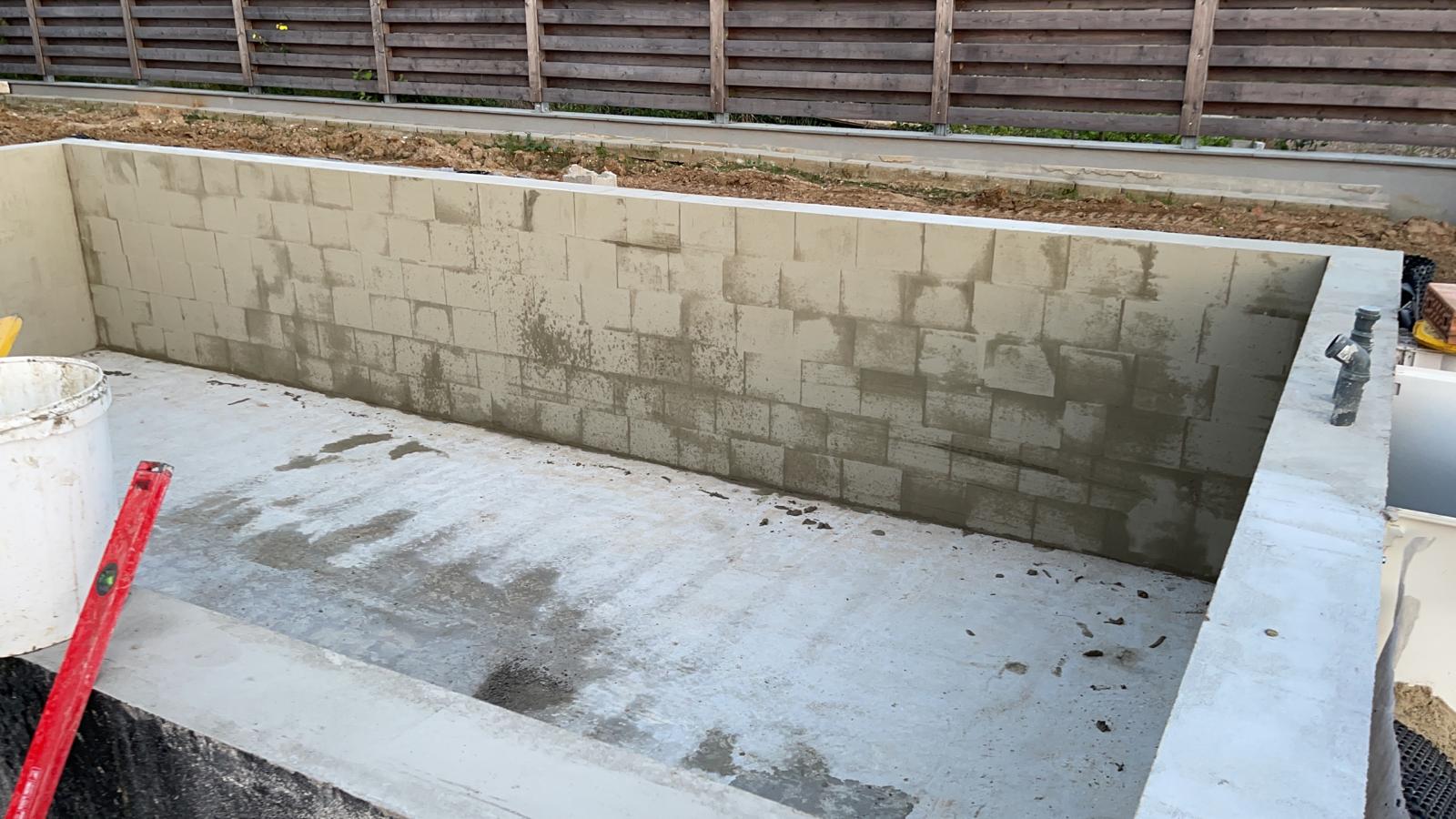 Im Bau befindliche Betonblockstruktur mit Zementboden, Holzzaun im Hintergrund.