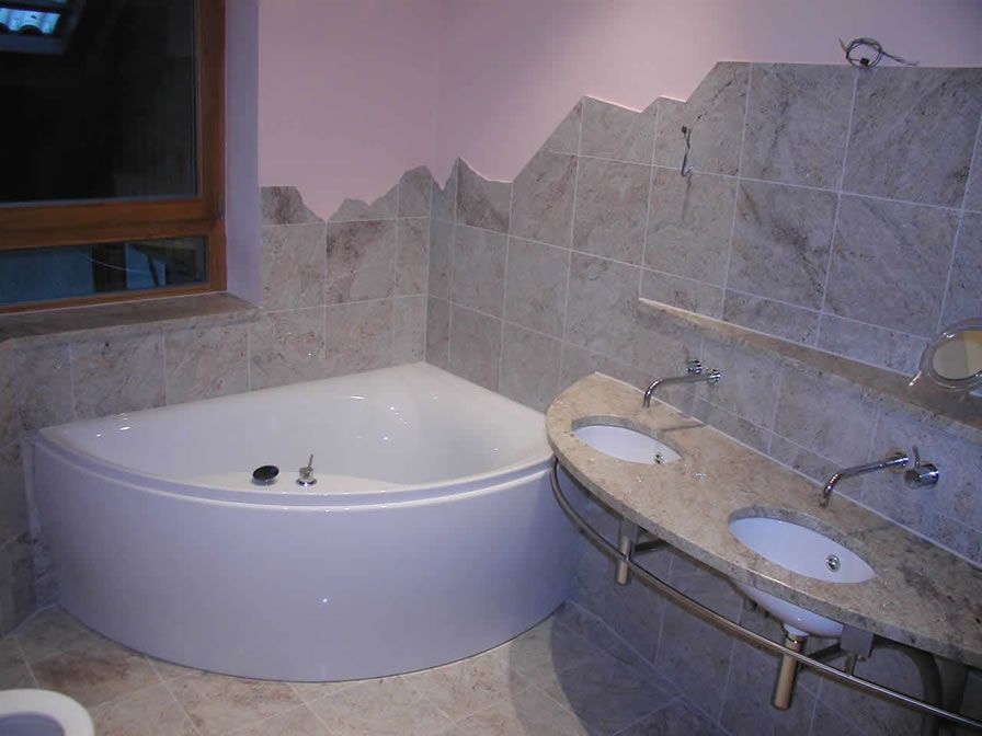 Badezimmer mit weißer Eckbadewanne, Doppelwaschbecken und Wänden aus Steinfliesen mit bergähnlichem Design.