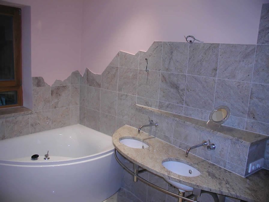 Badezimmer mit weißer Badewanne, Doppelwaschbecken und hellgrauen Fliesen. Die rosa Wand hat einen bergähnlichen Rand.
