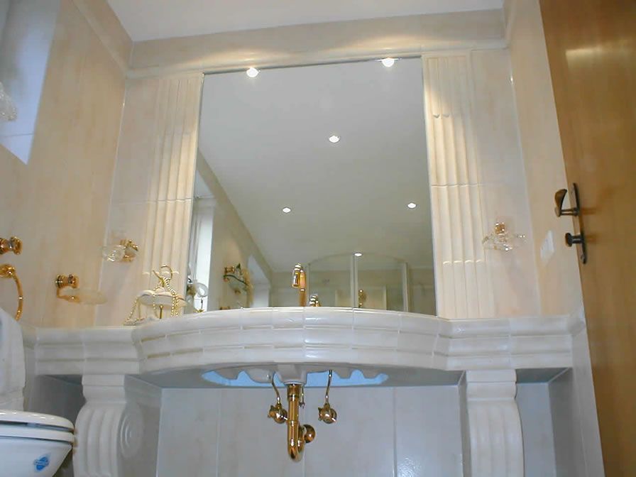 Badezimmer mit goldenen Armaturen, verziertem Waschbecken, großem Spiegel und Fliesenumrandung.