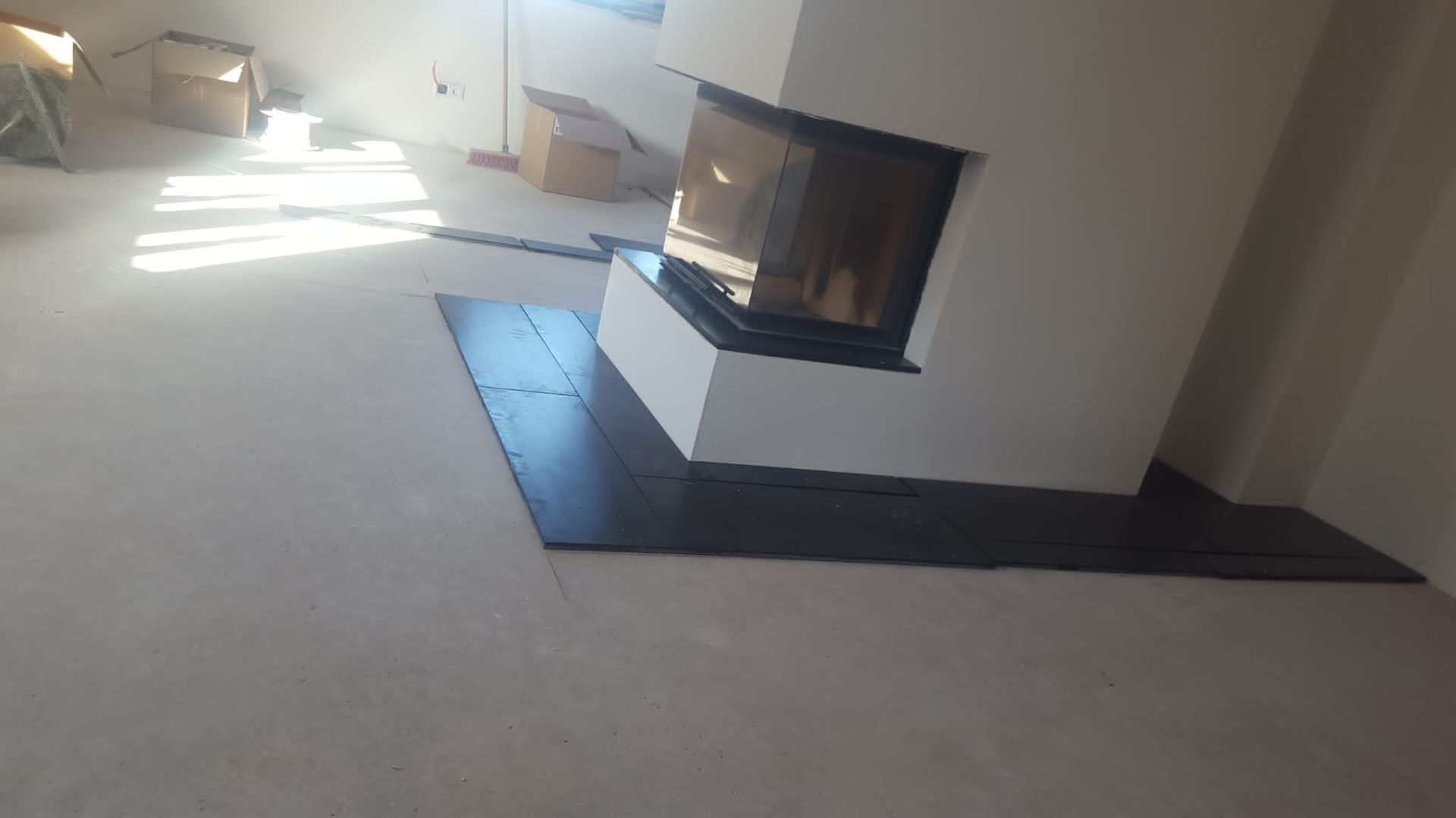 Kamin mit schwarzer Steinplatte in einem hellen Raum. Sonnenlicht strömt über den Boden.