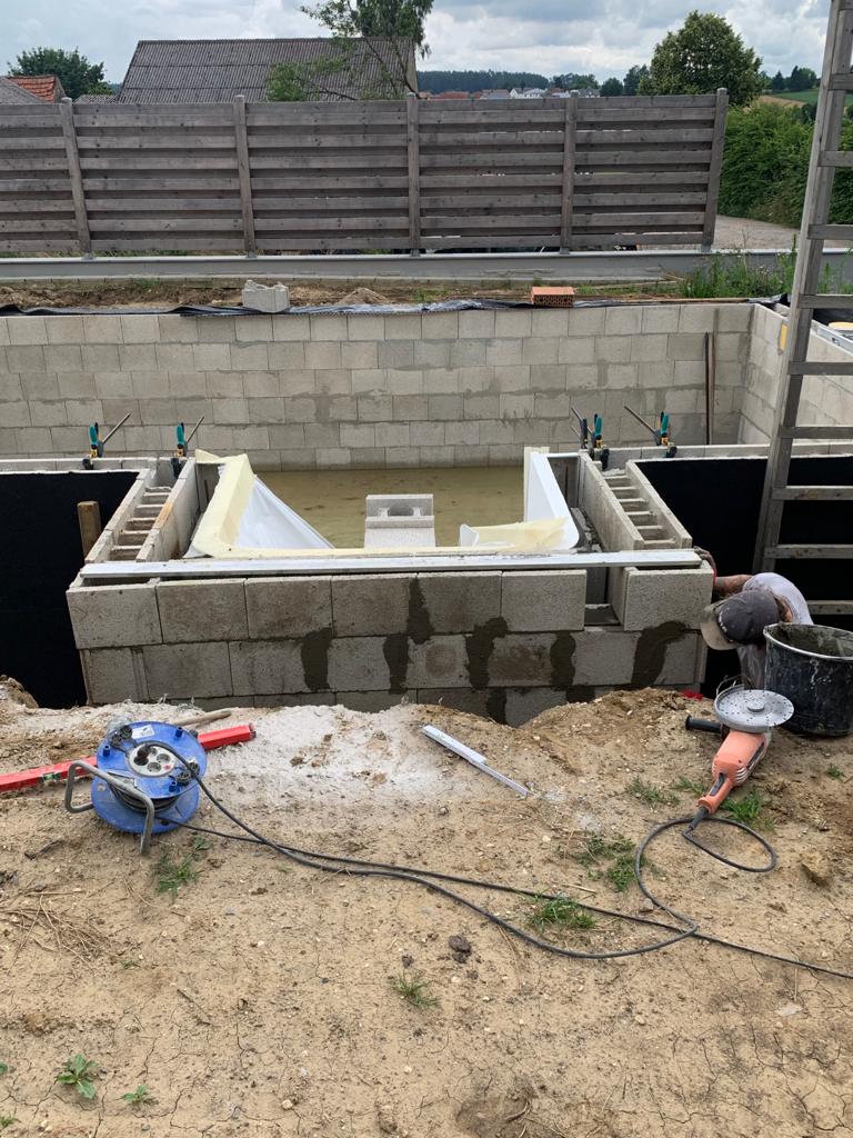 Baustelle: Eine Blockmauer wird um einen Poolbereich herum errichtet. Ein Arbeiter schleift Beton.