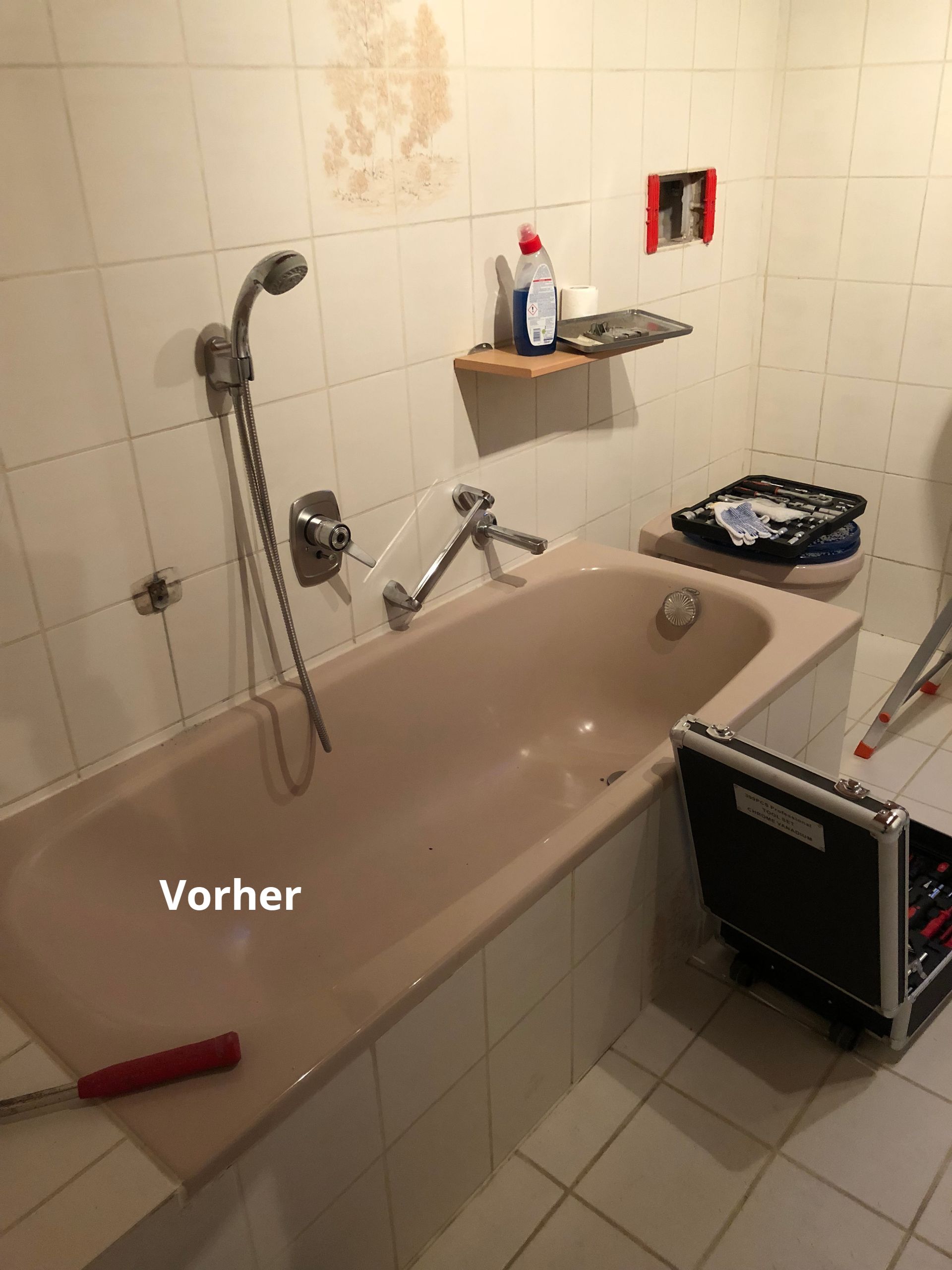 Badezimmer vor der Renovierung: rosa Badewanne, Fliesen, Regal mit Putzmitteln, offener Werkzeugkasten. Bildunterschrift „Vorher“.