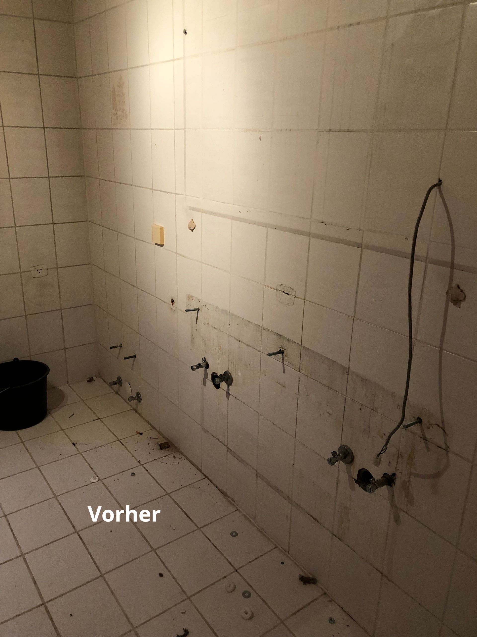 Schmutziger, gefliester Raum mit freiliegenden Rohren und einem Eimer. Unten links Etikett „Vorher“.
