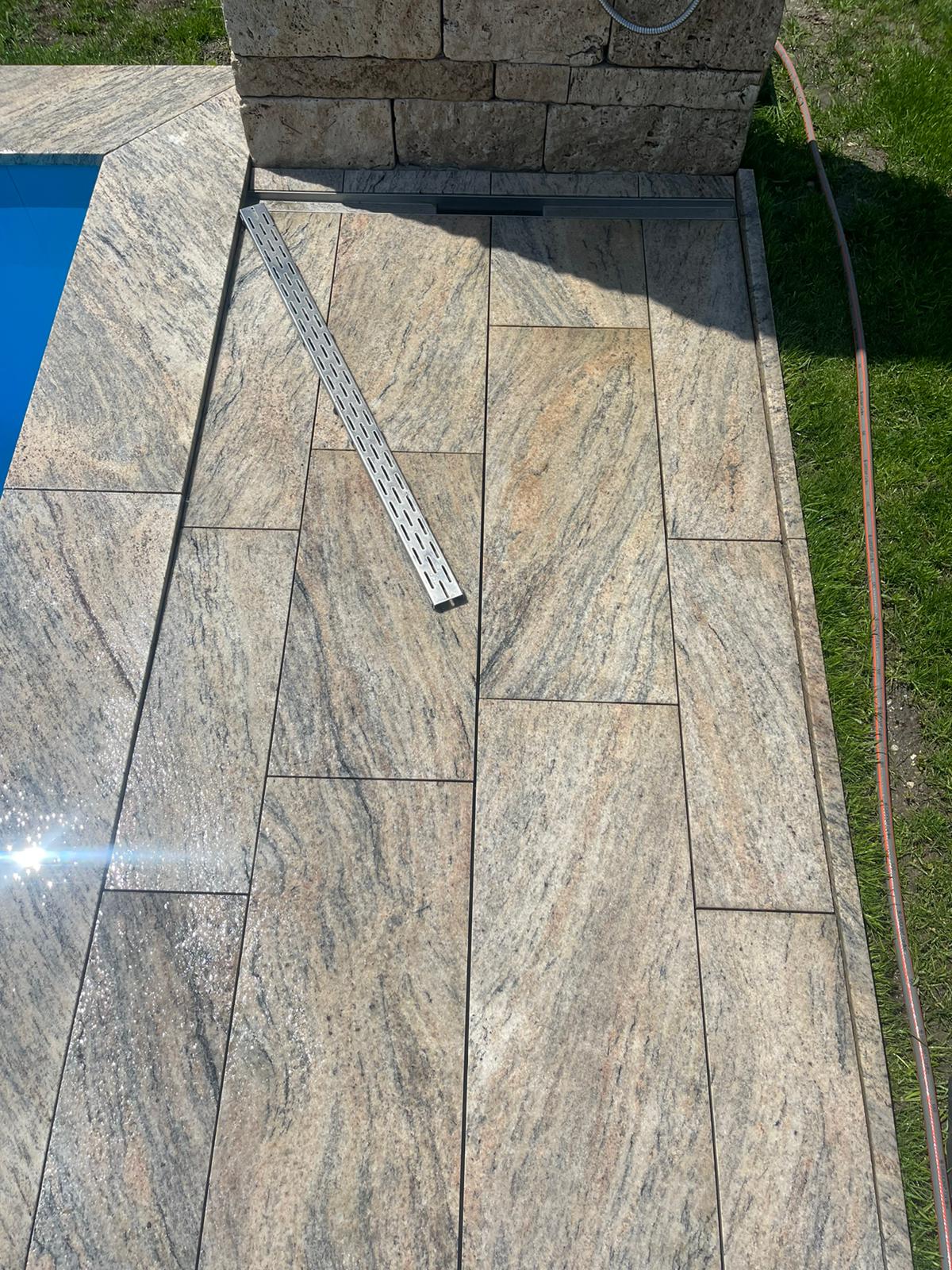 Steinterrasse um einen Pool mit Lineal, Gras und Steinsäule.
