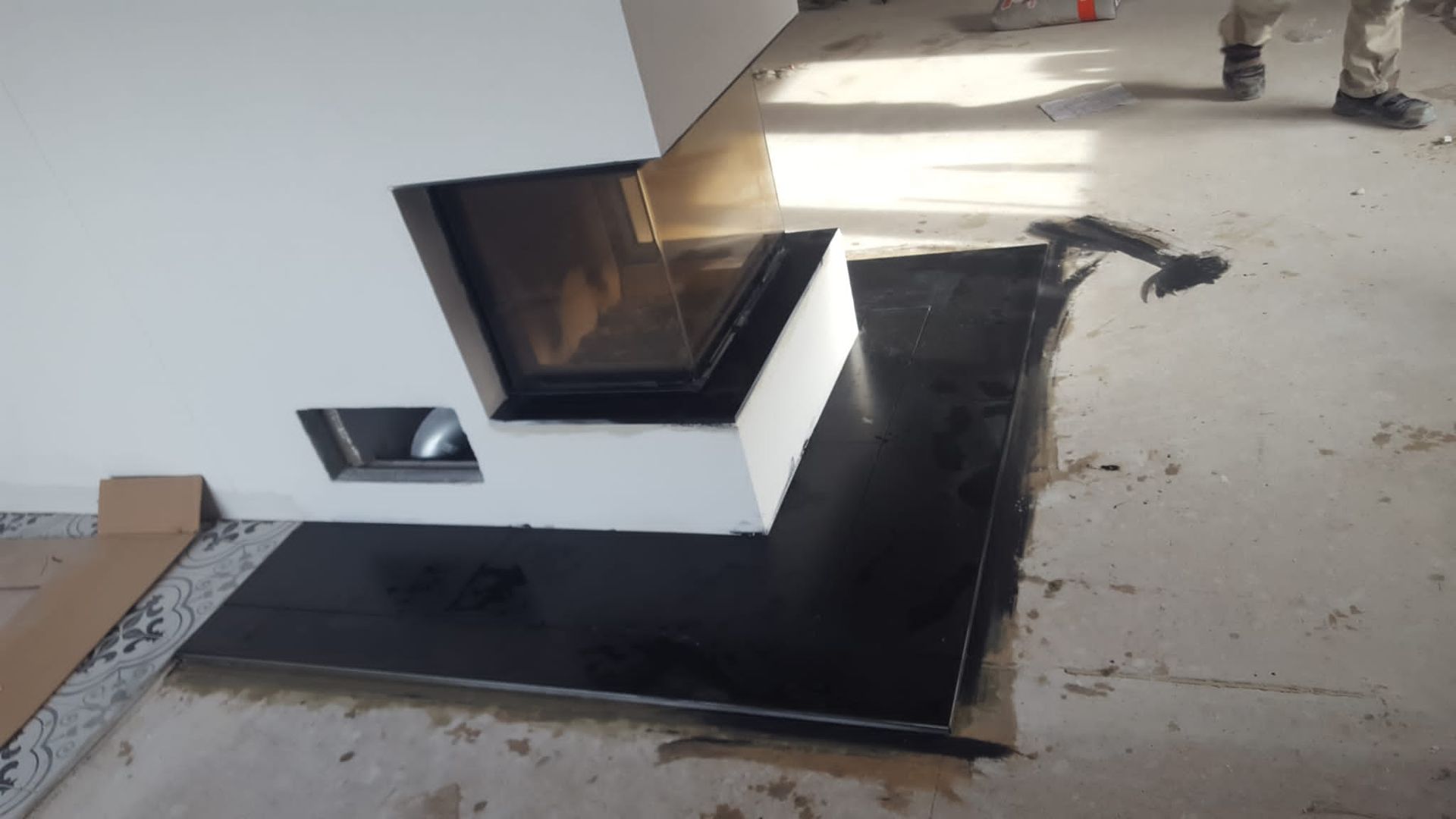 Weißer Kamin mit schwarzer Feuerstelle vor weißer Wand.