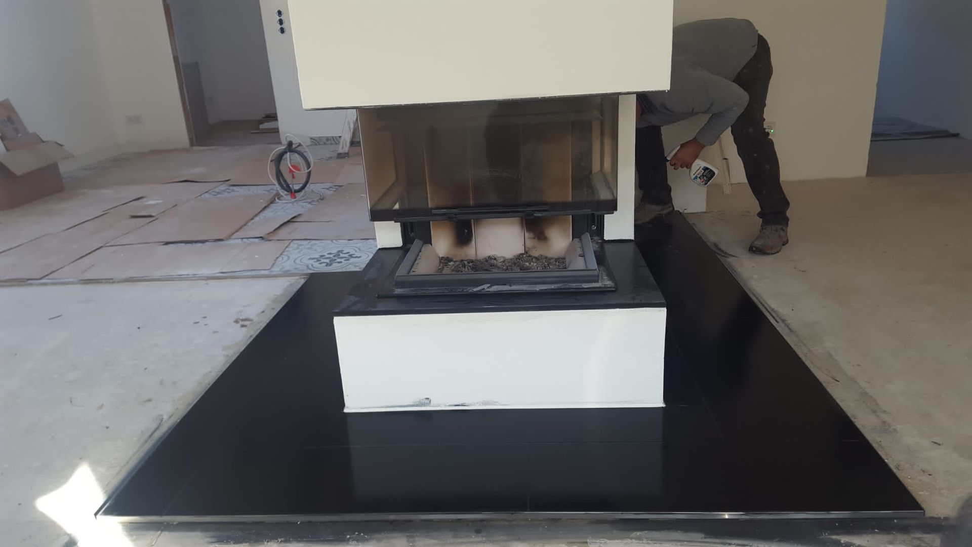 Eine Person reinigt einen Kamin. Eine weiße Einfassung sitzt auf einem schwarzen Sockel in einem Raum im Umbau.