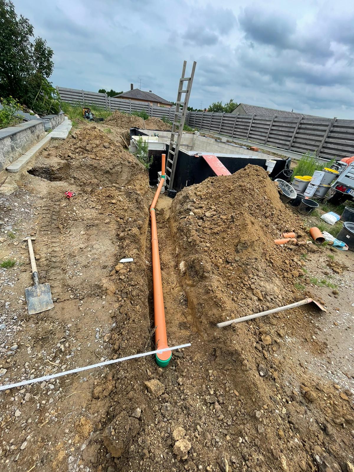 Orangefarbenes Abflussrohr im Graben, Baustelle, Leiter, Erdhaufen, bewölkter Himmel.