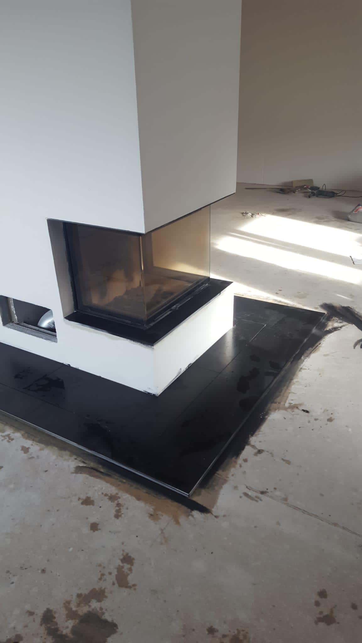 Moderner weißer Kamin mit schwarzer Feuerstelle auf einem Betonboden in einem unfertigen Raum.