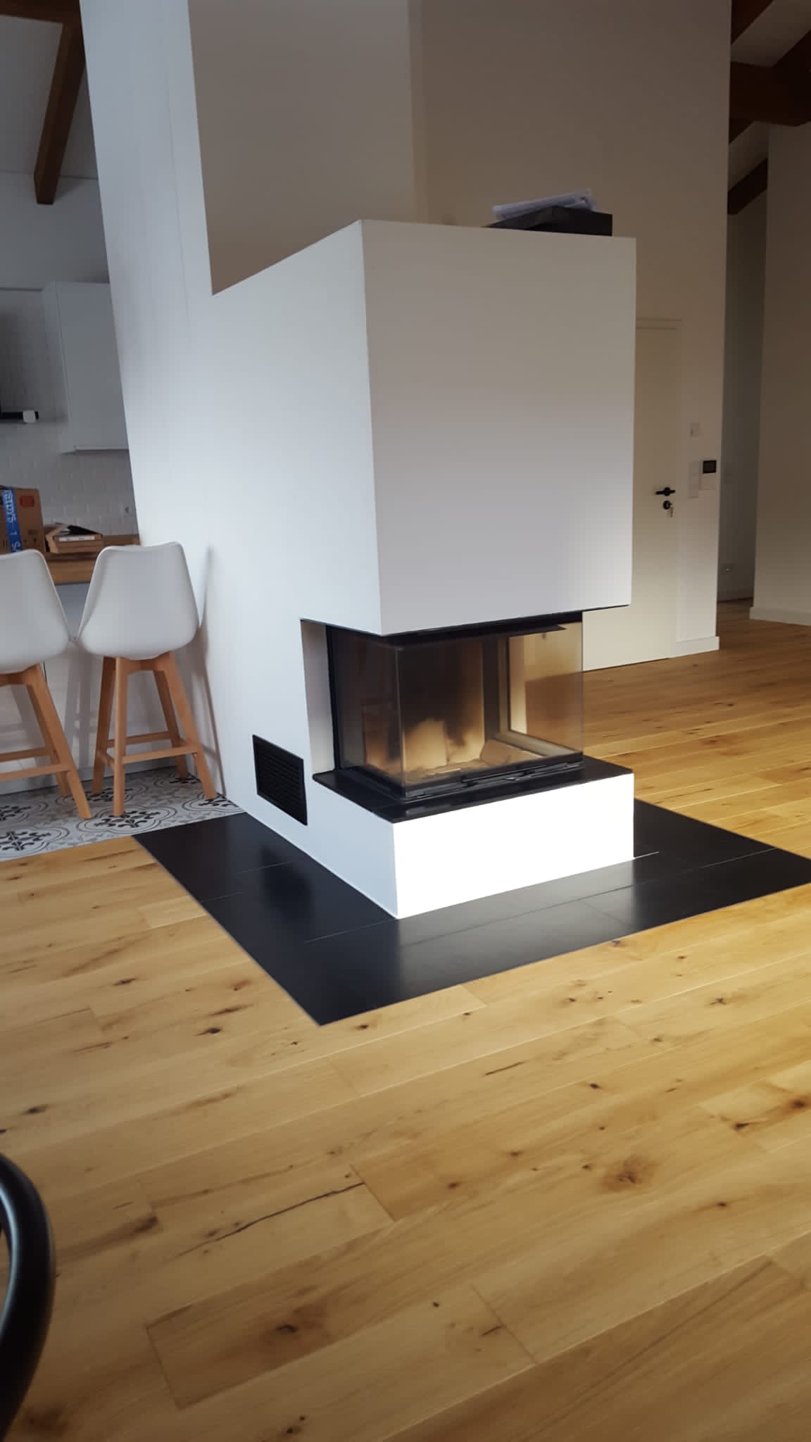 Moderner weißer Kamin mit schwarzer Feuerstelle auf Holzboden.