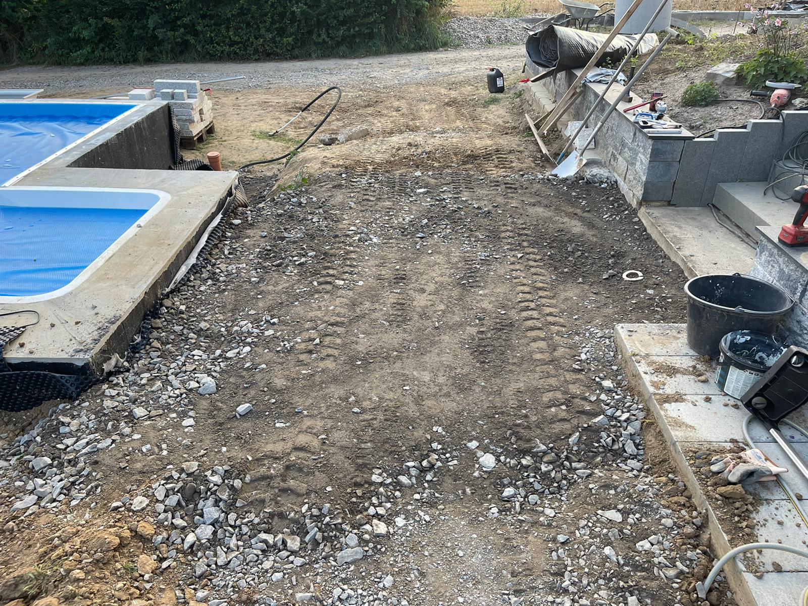 Baustelle mit freiliegendem Boden, einem Pool mit blauer Abdeckung und einer Betonmauer.