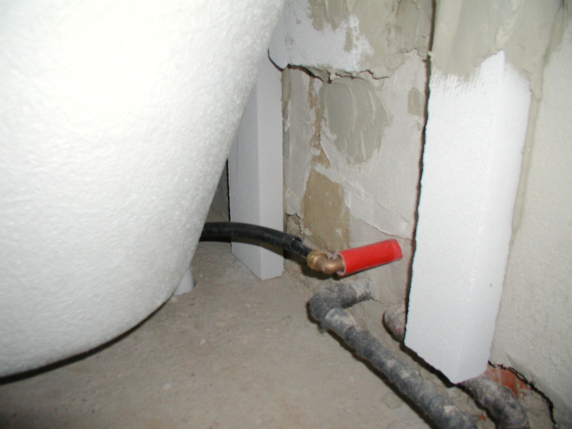 Eine Badewanne und teilweise freiliegende Wasserrohre in der Nähe einer Wand in einem Badezimmer; schwarze und rote Rohre.