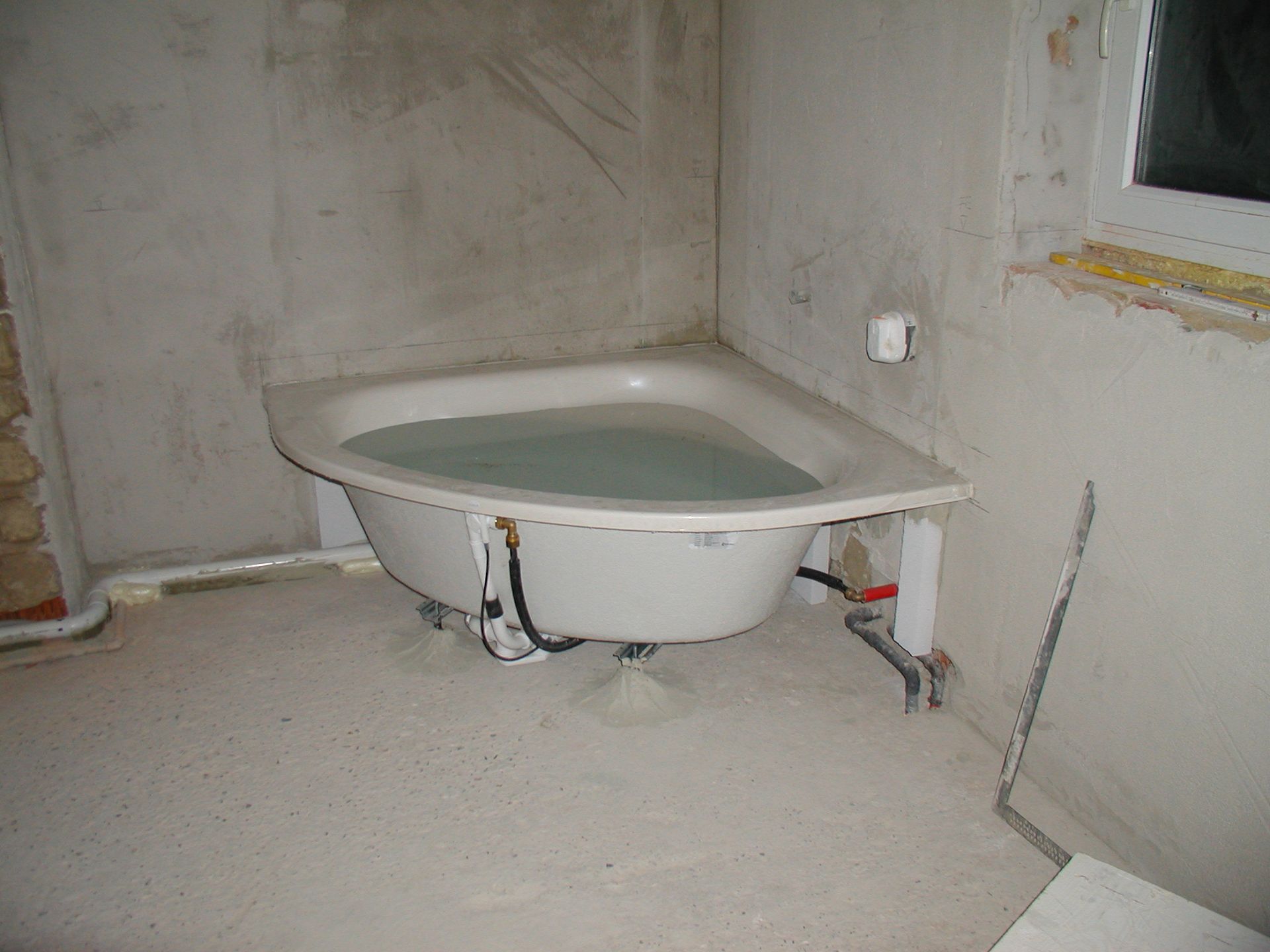 Mit Wasser gefüllte Eckbadewanne in einem im Bau befindlichen Raum mit unfertigen Wänden und Boden.